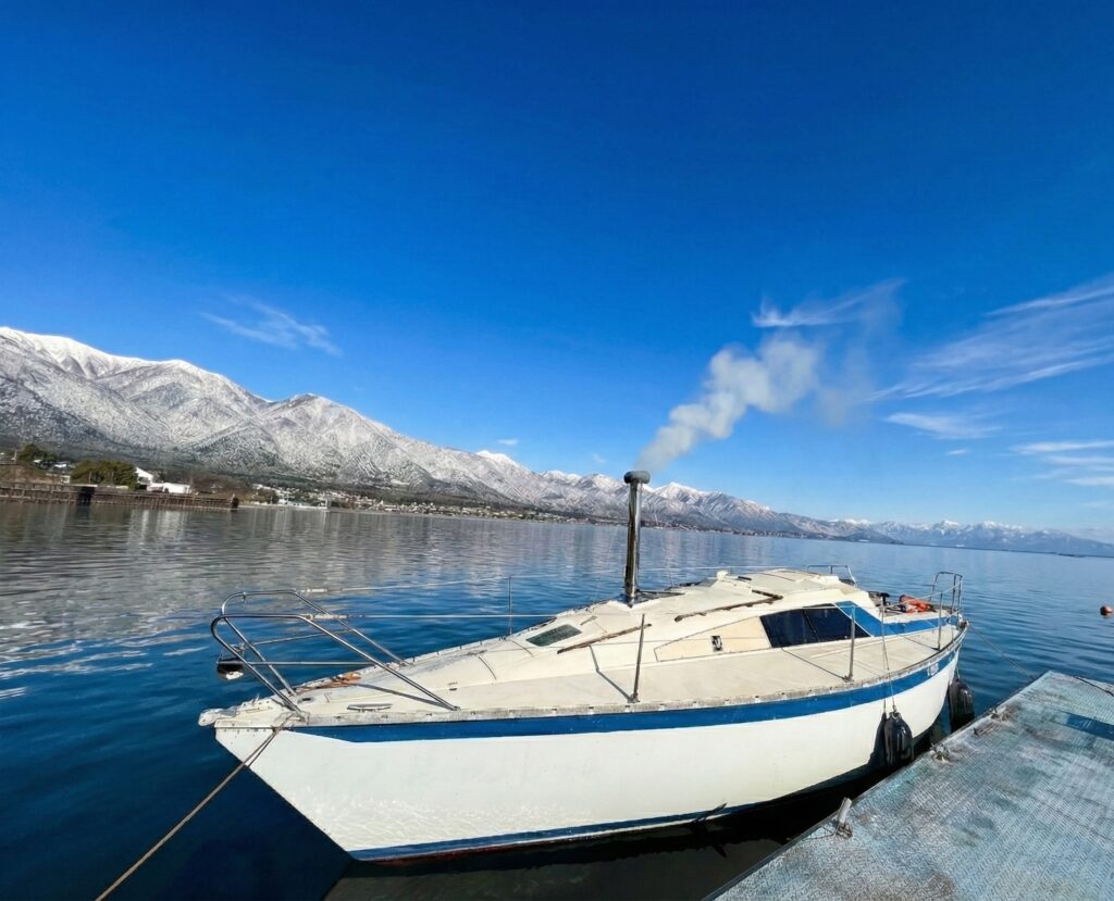 雪化粧した比良山系を背景に、煙突から煙を上げる琵琶湖のヨットサウナ