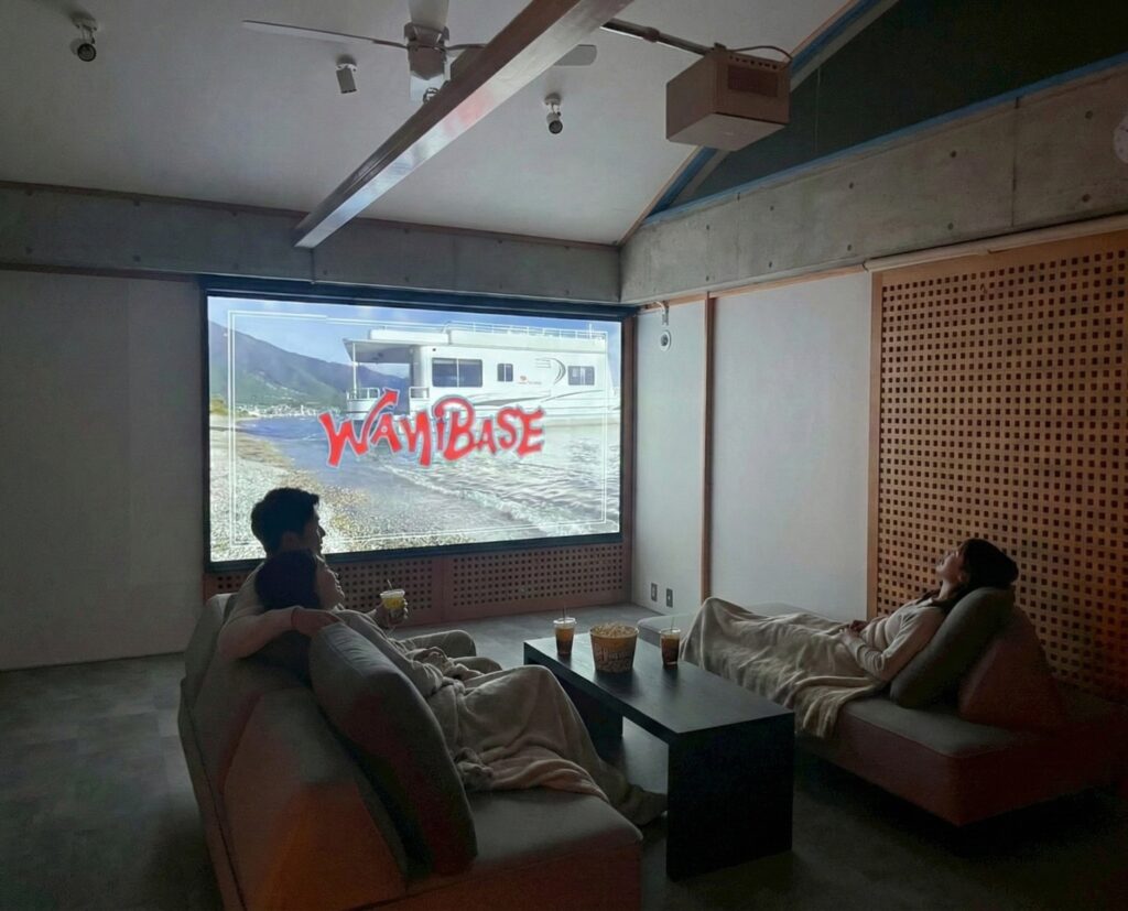 滋賀の貸別荘Star Houseのリビング。120インチ巨大スクリーンとプロジェクターで映画鑑賞を楽しむカップルとグループ。